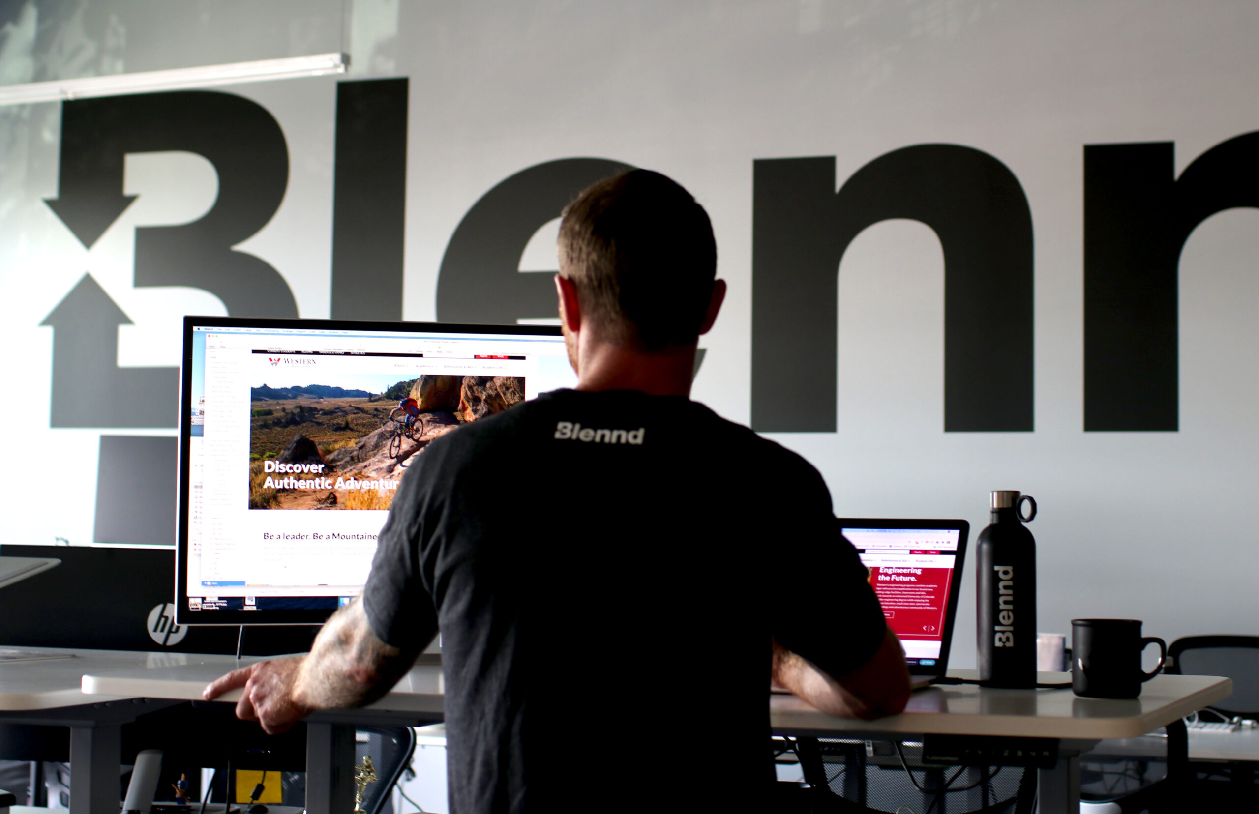 Team member working at desk with Blennd logo wall behind